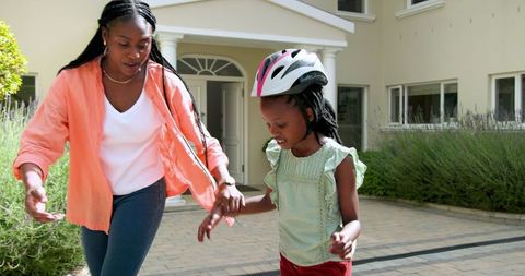 Mother teaching daughter to ride bicycle outside home in sunny day