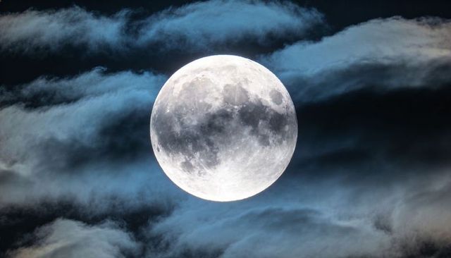 Full moon glowing through bluish clouds revealing lunar craters and maria