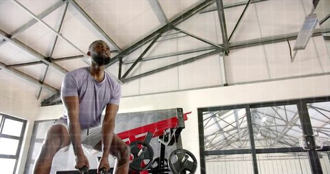 Athletic man lifting heavy dumbbells in industrial gym performing focused deadlift