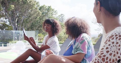 African american friends sharing tablet on pool deck relaxing in crochet cover-ups