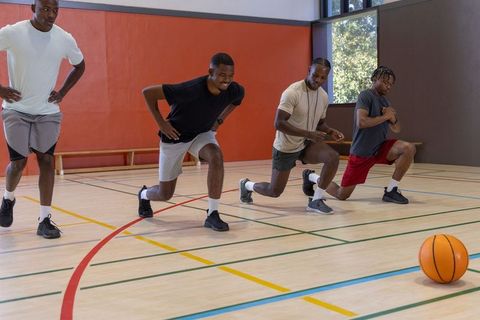 African american men performing lunges in gymnasium warming up for basketball training