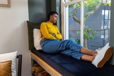 African american woman reclining on window bench, gazing outside in cozy home nook