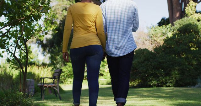 Rear view of african american couple holding hands and walking in sunny garden. staying at home in isolation during quarantine lockdown.