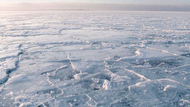 Stretching frozen sea ice sheets revealing surface cracks and snow ridges at arctic horizon