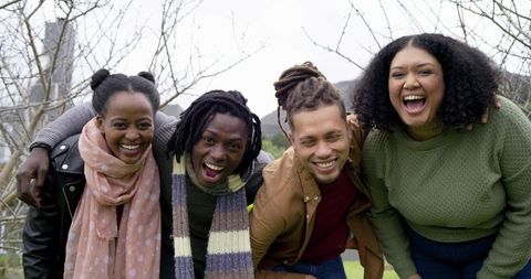 Multiracial friends laughing with arms linked outdoors on overcast day sharing joy