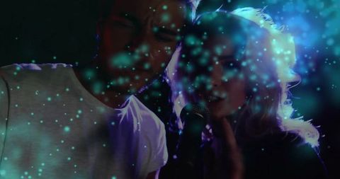 Singing duo sharing microphone with teal glow on stage