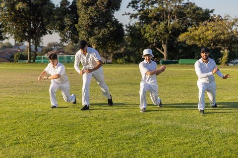 Cricket players lunging in synchronized fielding drill on grassy ground during golden hour