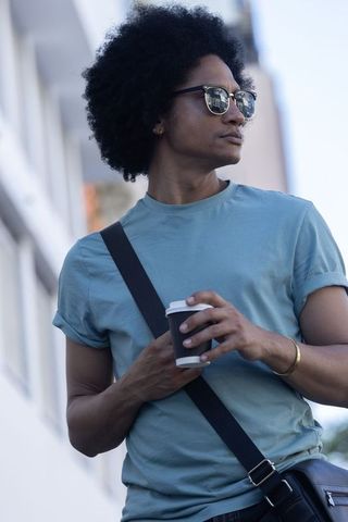 Urban african american man holding coffee, wearing mirrored sunglasses and crossbody bag