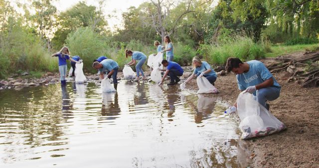 Group of volunteers cleaning a riverbank, collecting trash from the water and adjacent land. Participants are focused on removing pollution and safeguarding the environment. Useful for promoting community service, environmental awareness initiatives, and conservation projects.