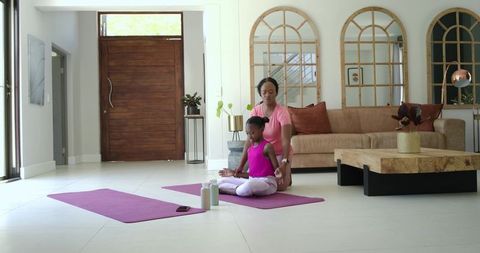 Mother guiding daughter practicing yoga and mindfulness in bright modern living room