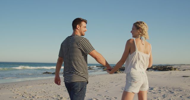 Happy caucasian couple walking and holding hands at beach on sunny day. Vacation, summer and lifestyle, unaltered.