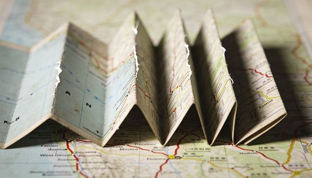 Displaying vintage road map folding into accordion folds on tabletop with creased texture