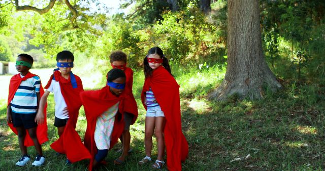 A diverse group of children dressed in superhero capes stands outdoors, ready for imaginative play, with copy space. Their vibrant costumes and playful stances evoke a sense of adventure and childhood fun.
