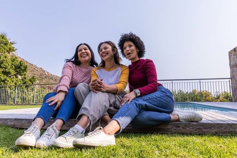 Multiracial friends laughing and relaxing on backyard deck by pool