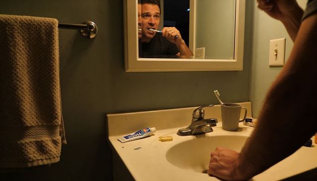 Middle-aged man brushing teeth at sink during nighttime personal hygiene routine