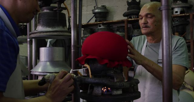 Two artisans are seen intensely focused on crafting red wool hats using traditional methods in a workshop. This image is excellent for use in articles or features about handicrafts, cultural heritage, or the preservation of traditional skills. It also suits marketing materials for artisan-made products or documentaries about cultural craftsmanship.