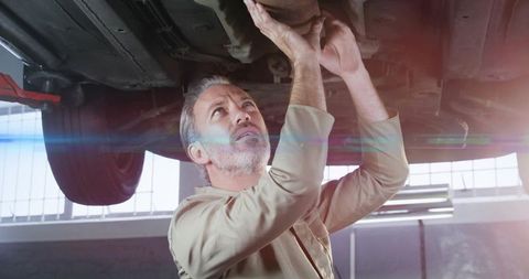 Experienced mechanic inspecting car undercarriage on lift in garage with muffler visible