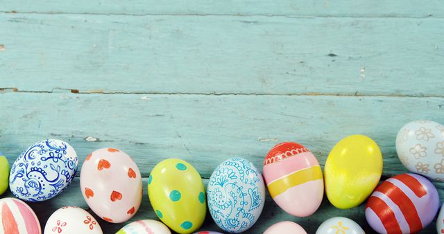 Colorful painted Easter eggs are lined up against a rustic blue wooden background, with copy space. These eggs symbolize the festive spirit of the Easter holiday and the tradition of egg decoration.