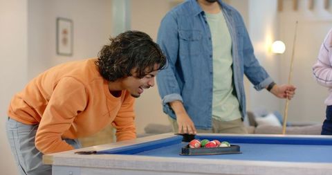 Friends leaning over blue-felt pool table lining up rack during casual home game night