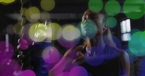 Female athlete gripping rope and holding water bottle, training with colorful bokeh lighting