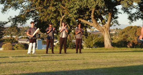 Cricket players celebrating victory on park field exchanging bats and gear at sunset