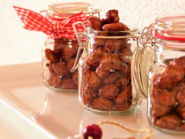 Homemade candied nuts packed in glass jars with decorative ribbon present visually appealing treat. Ideal for holiday gifts, festive celebrations, DIY projects, and food blog illustrations. Suitable for advertising homemade food products or showcasing crafting skills.