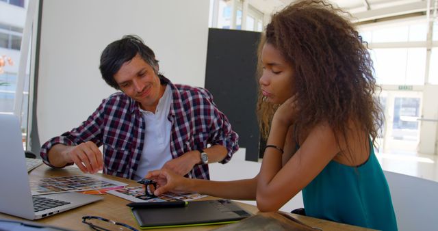 Caucasian man mentors a teenage African American girl at the office. They are collaborating on a creative project, surrounded by technology and design elements.