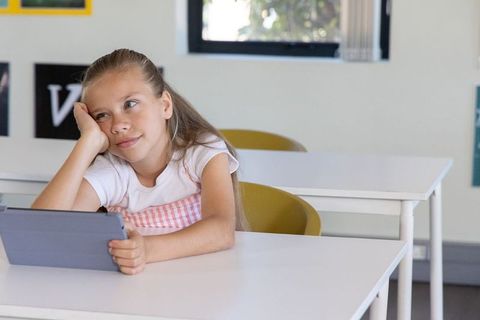 Thoughtful girl using tablet in classroom, daydreaming and exploring digital learning