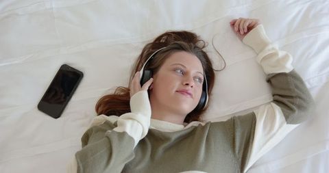 Young Woman Relaxing on Bed Listening to Music on Headphones
