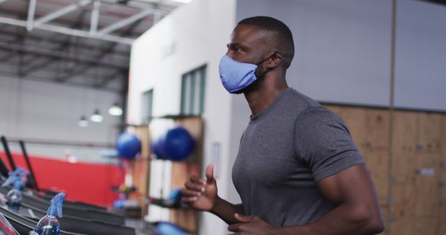 Man running on treadmill in gym wearing a mask. Ideal for illustrating fitness, health precautions during the COVID-19 pandemic, and gym workouts.