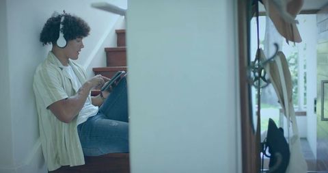 Young man listening to music using tablet on wooden stairs with headphones