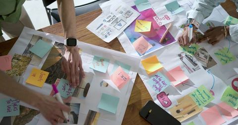 Creative team brainstorming with colorful sticky notes on wooden table for design planning