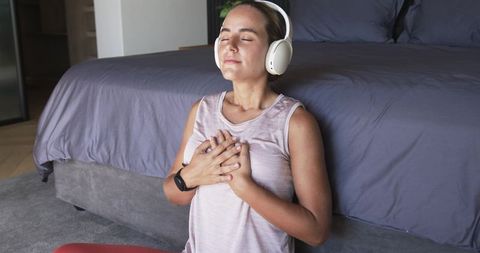 Young woman practicing mindfulness with headphones in cozy minimalist bedroom during meditation