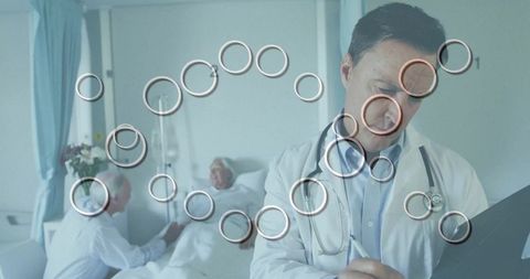 Doctor writing bedside notes while senior patient receives care and companion supporting