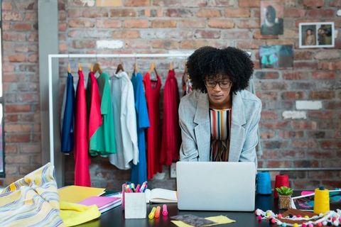 Fashion Designer Optimizing Clothing Production on Laptop