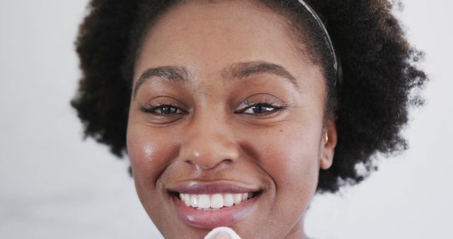 Smiling Afro-American woman cleansing her face with cotton pad - Download Free Stock Images Pikwizard.com