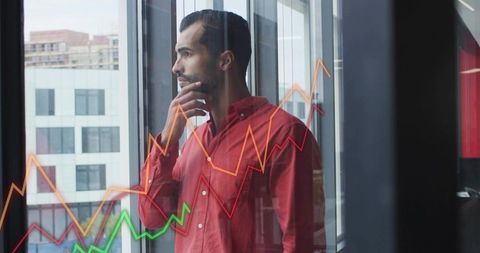 Man analyzing financial graphs at office window