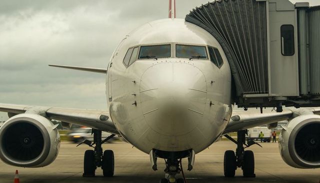 Docking commercial jet at gate with boarding bridge and ground crew on tarmac, front-view