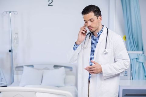 Confident male doctor using mobile phone beside hospital bed