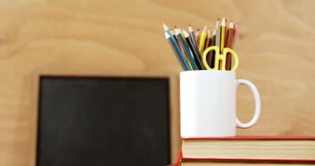 Books stacked with white mug holding pencils and scissors, suitable for promoting educational content, blog posts about organization and study habits, back-to-school advertisements, or teacher resources.