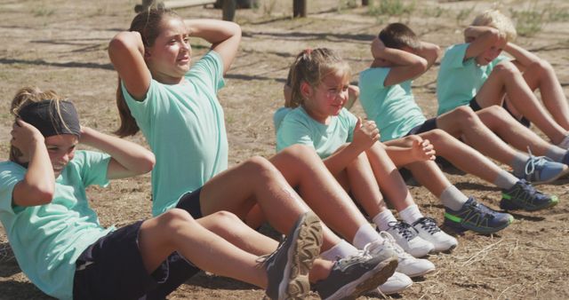 Group of children doing sit-ups outdoors, engaging in fitness activities. Use for content related to children's fitness, group exercises, healthy lifestyle, summer camps, physical education programs, and teamwork activities.