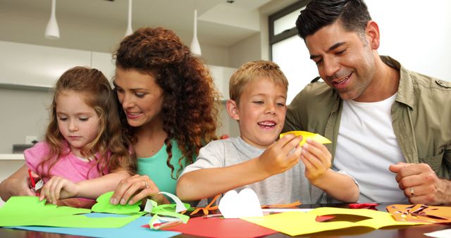 Parents and two children, a boy and a girl, engaged in a creative arts and crafts project at home. Suitable for use in articles or advertisements about family bonding, creative activities, and parental involvement in children's development.
