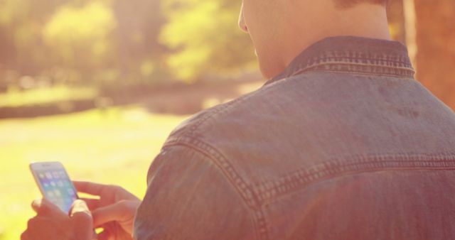 Person holding and using a smartphone outdoors with sunlight in the background. Good for illustrating modern technology use, mobile communication, or outdoor activities.