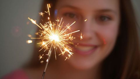 Handheld Sparkler Glowing Close-Up with Blurred Smiling Woman Holding Festive Glow Indoors