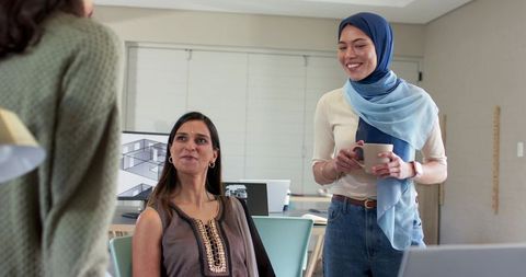 Diverse female team collaborating on architecture renderings with hijab-wearing colleague