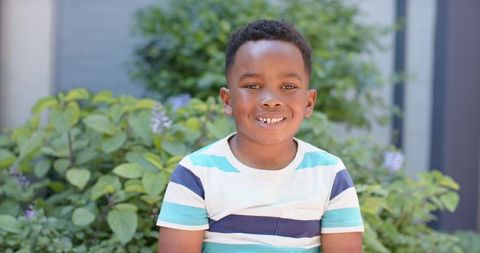 African american boy smiling and looking at camera in sunny courtyard with green foliage