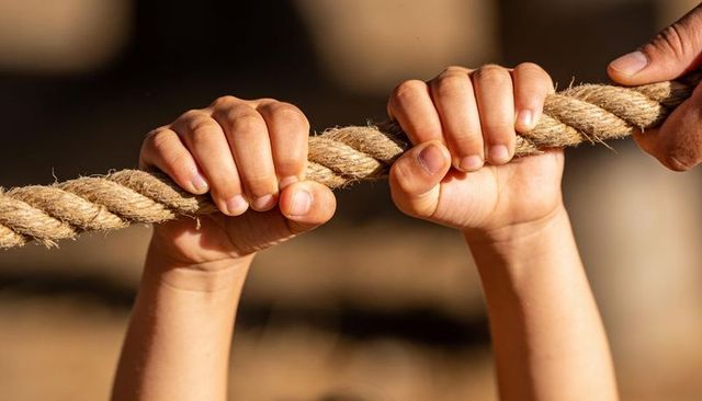 Child and adult hands gripping braided rope during playground tug under warm sunlight
