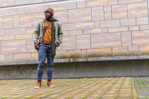 African american man standing on urban plaza wearing beanie scarf jacket and crossbody