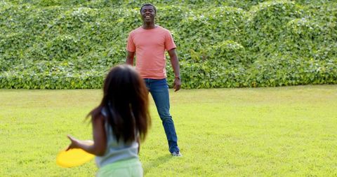 Father and Daughter Playing Frisbee on Bright Lawned Yard