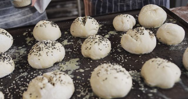 Unbaked dough balls topped with black and white sesame seeds on a baking tray. Ideal for projects related to baking, bread making, food preparation, and culinary education. Useful for blog posts, recipe books, and cooking courses that emphasize the process of baking and artisanal bread.
